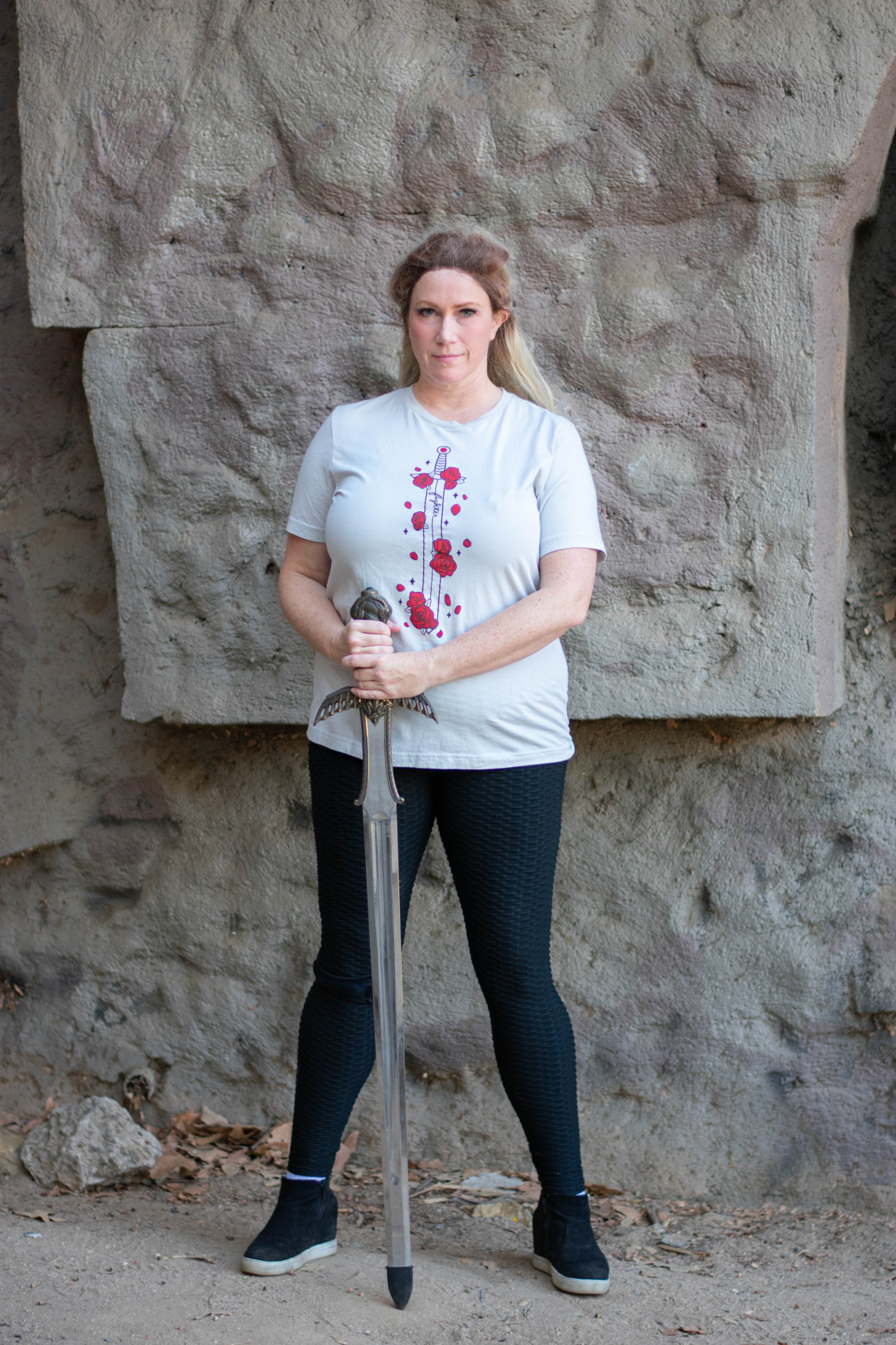 A model poses with a sword while wearing a tee featuring a sword covered in red flowers by D%D fashion brand Guild Party.