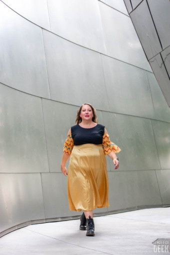 A model walks in front of the reflective walls of the Walt Disney Concert Hall. She wears a gold skirt and a ruffle sleeve top by Heroicouture. 