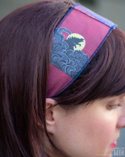 A closeup of a model wearing a headband with a Kaiju print inspired by Godzilla. 