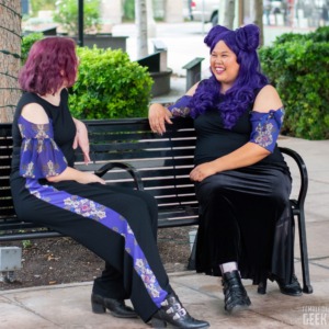 Two models chat while sitting on a bench. 