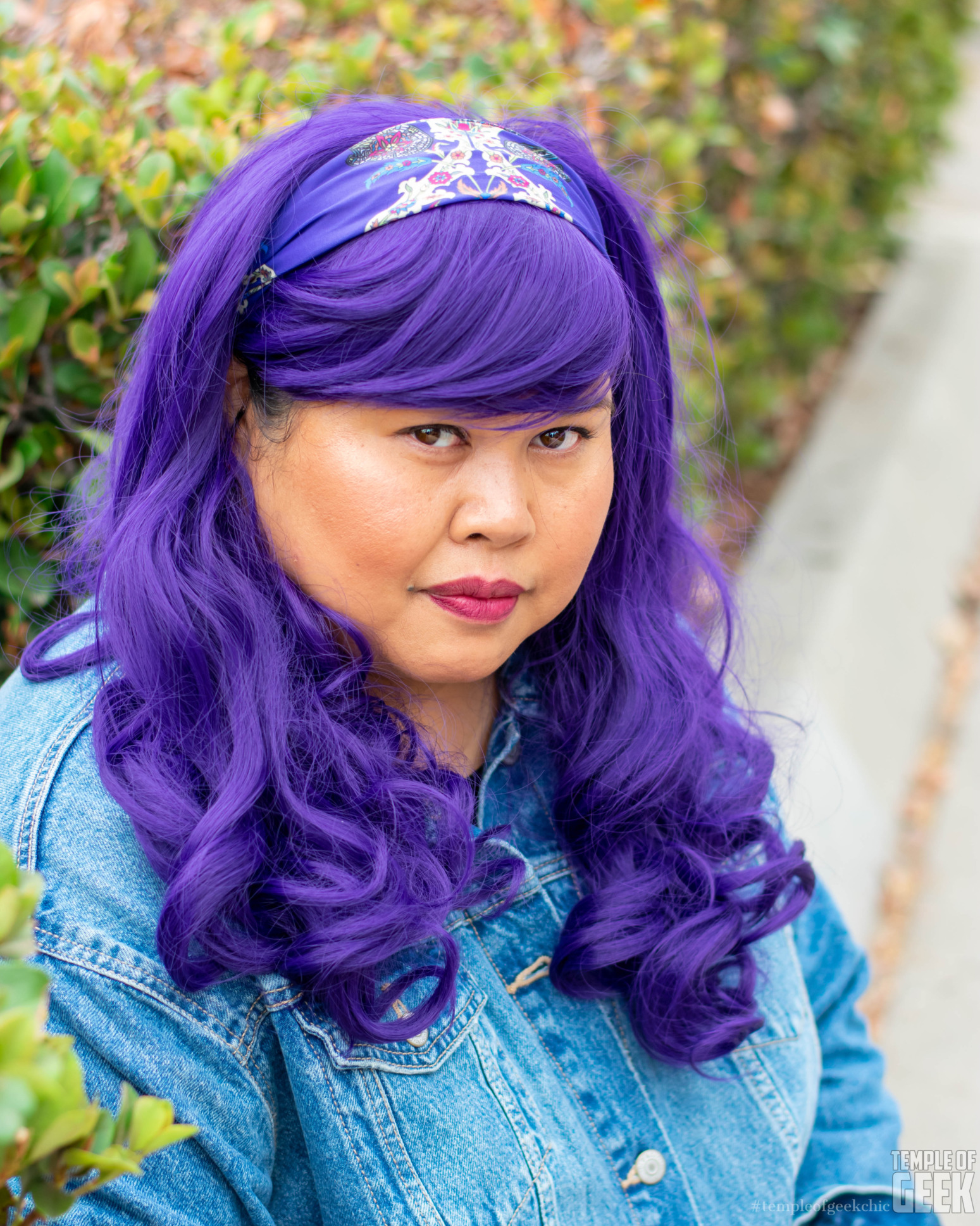 Closeup of a model wearing a purple wig and matching headband.