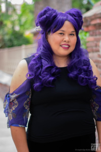 A model wears a purple wig, which matches her ruffle sleeve top by Heroicouture. 