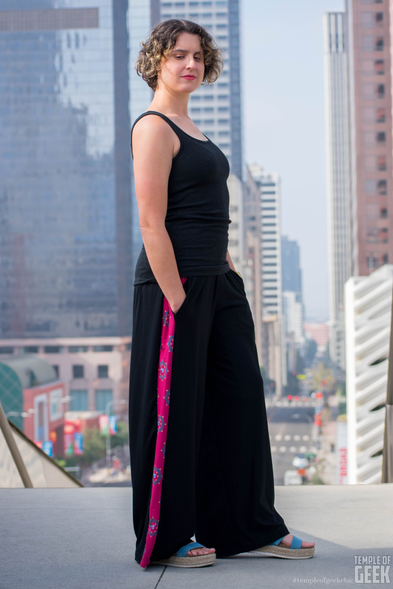 A model wears palazzo pants with a print inspired by Wonder Woman and stands in front of the downtown LA skyline. The pants are part of a collection by Heroicouture inspired by Marvel and DC superheroes.