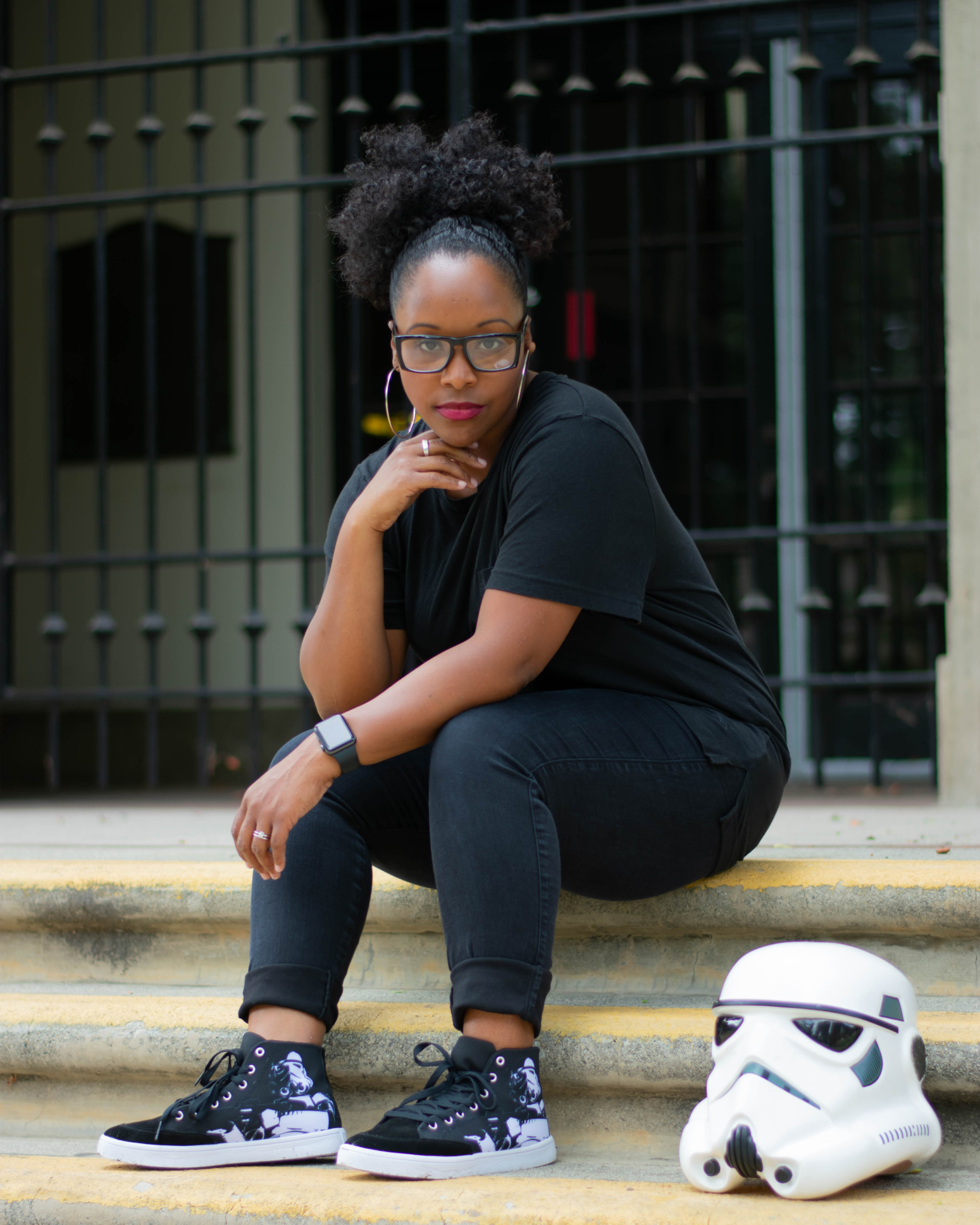 A model wears high top sneakers with Stormtroopers on them. A Stormtrooper helmet rests near her feet.