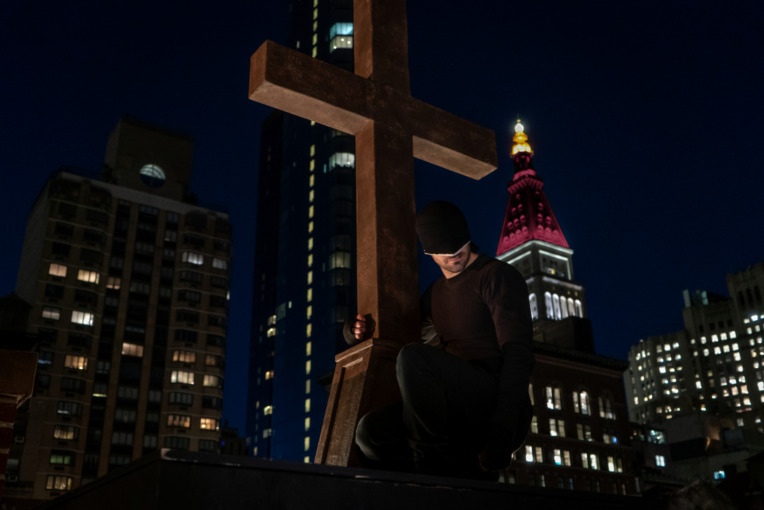 Daredevil perched next to cross on Rooftop