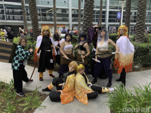 A group of Demon Slayer cosplayers standing with weapons drawn while surrounding two Zenitsu cosplayers who are "sleeping" back-to-back