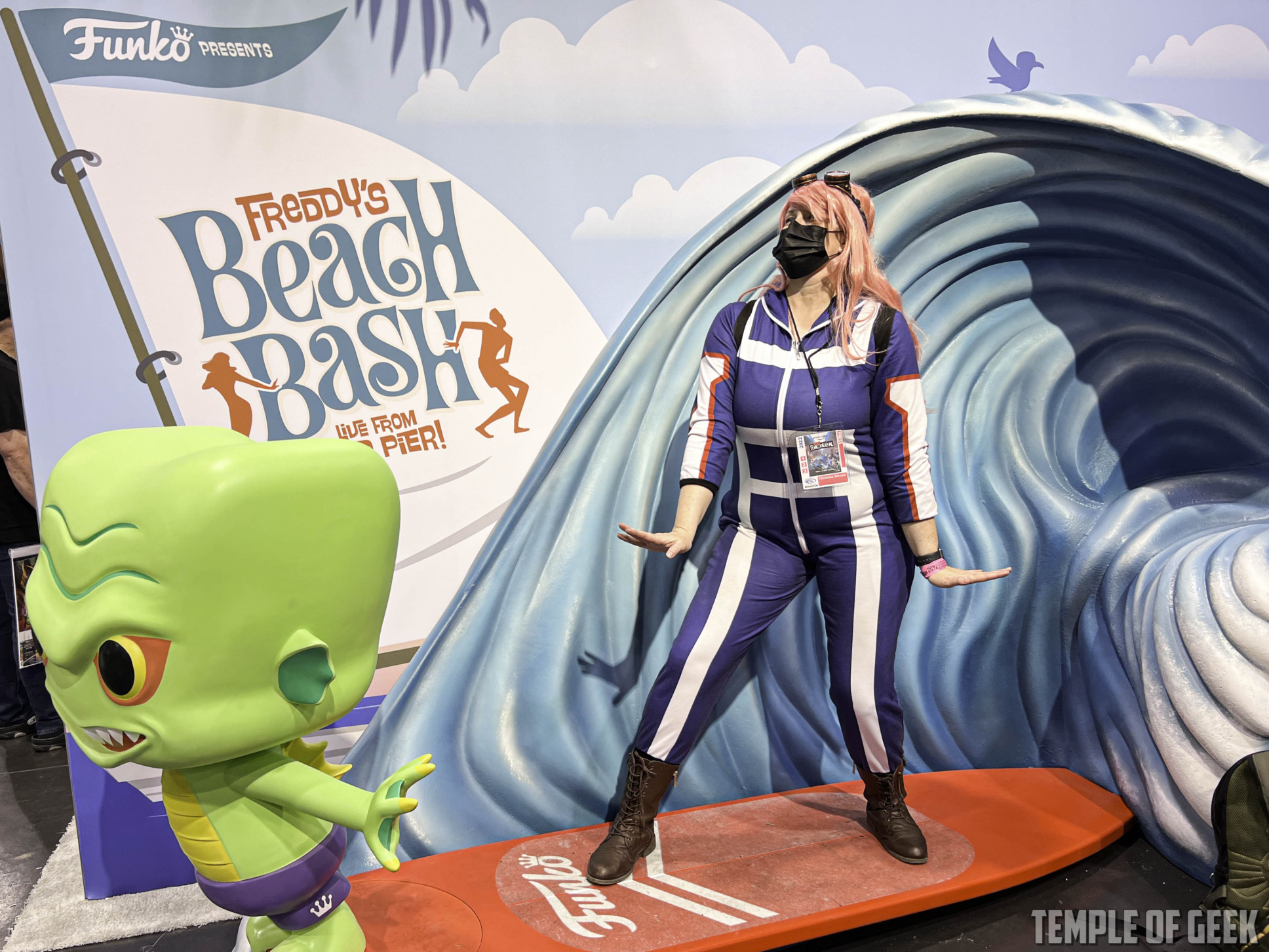 Cosplayer @Christina.is.crafty (on Instagram) at the Funko Pop Booth, she is dresses in a My Hero Academia Cosplay of Mei Hatsume. She is riding a fake surfboard at the Funko Booth exhibit