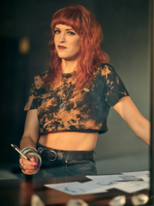 RockLove Jewelry founder and CEO stands at a desk, holding a pencil with some of her design pages in front of her. 