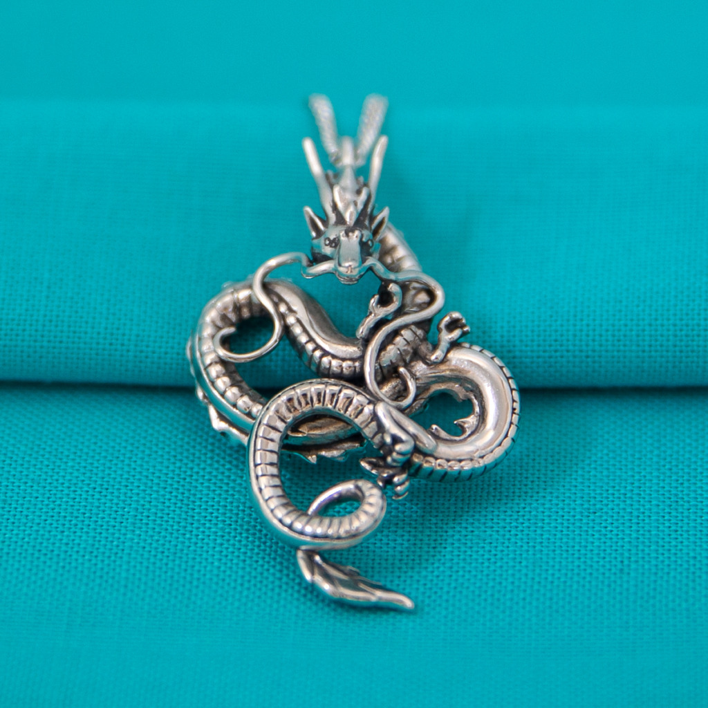 A sterling silver dragon pendant against a blue background. 