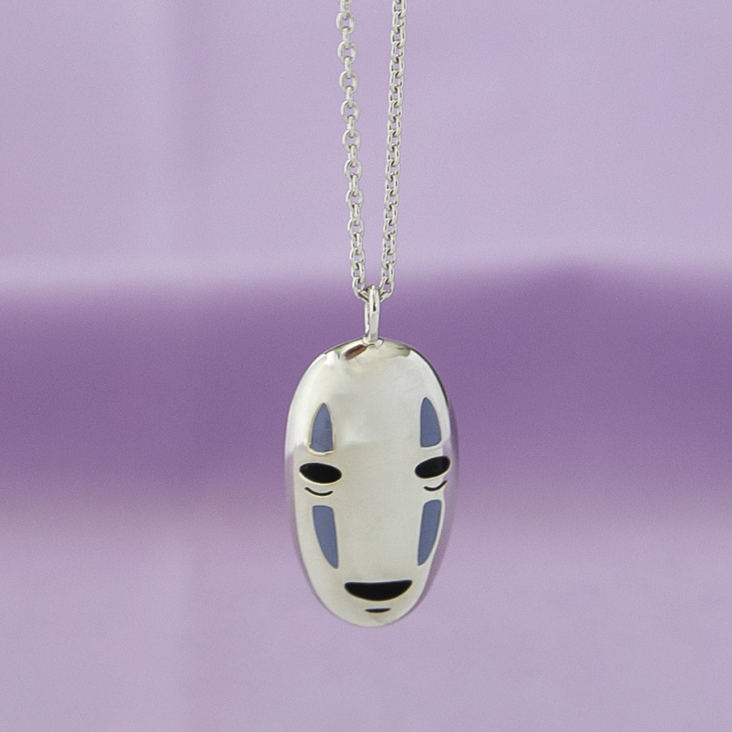 A sterling silver No-Face Necklace dangles from a chain in front of a purple background. 