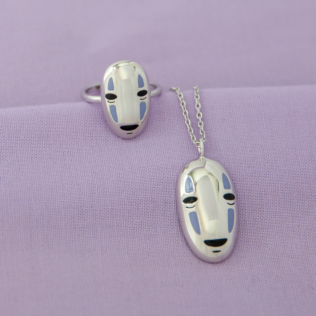 A No-Face necklace and No-Face ring against a purple backdrop. 