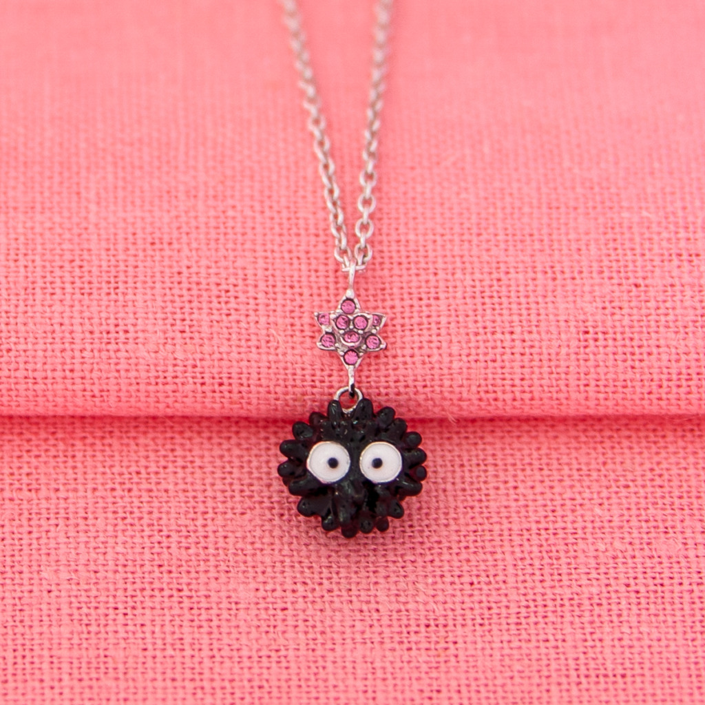 A Soot Sprite Necklace with a black enamel Soot Sprite and pink pave crystal candy star against a pink background.