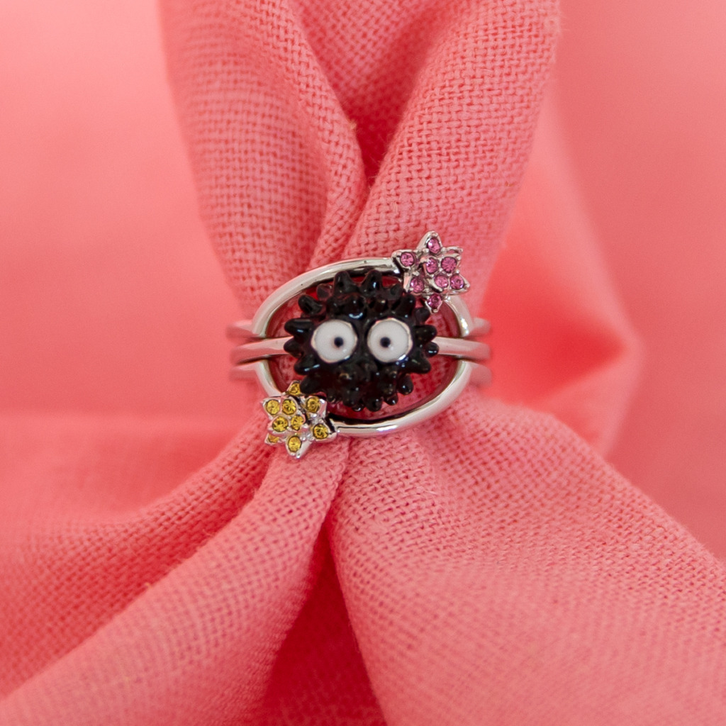 A Soot Sprite Stacker Ring with a black enamel Soot Sprite and pave crystal candy stars against a pink background.