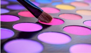 A makeup palette of pinks and purples with a makeup brush