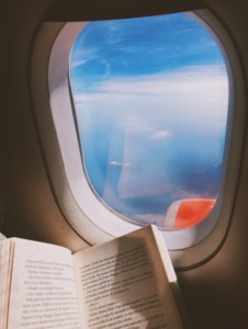 Someone reads a book while looking out the window of a plane