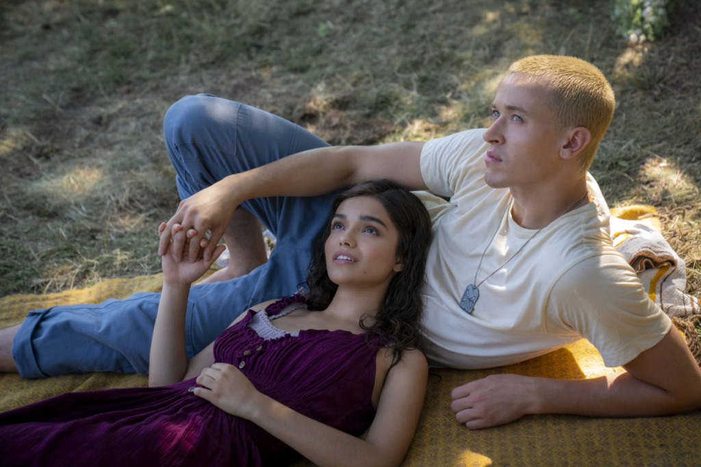 Rachel Zegler as Lucy Gray Baird and Tom Blyth as Coriolanus Snow in The Hunger Games: The Ballad of Songbirds and Snakes. They are laying down in field and Lucy Gray Baird is resting her head against Coriolanus Snow.