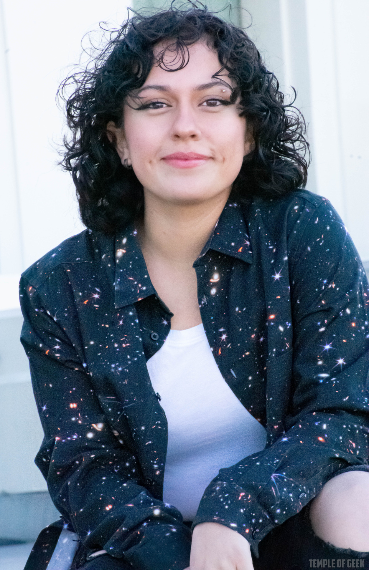 Closeup of a model smiling and wearing a black, space-themed button-up shirt over a white tanktop at Griffith Observatory.