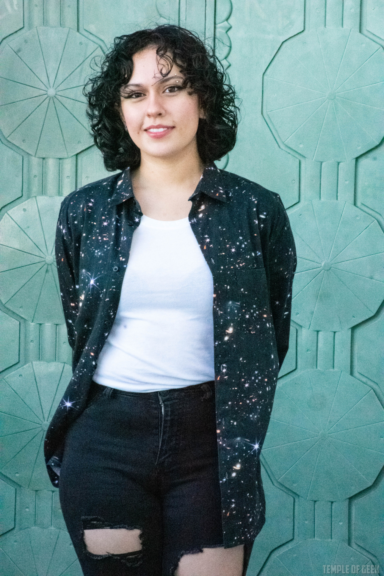 A model stands in front of a green art deco door at Griffith Observatory. She wears a button-up shirt over a black tanktop and jeans.