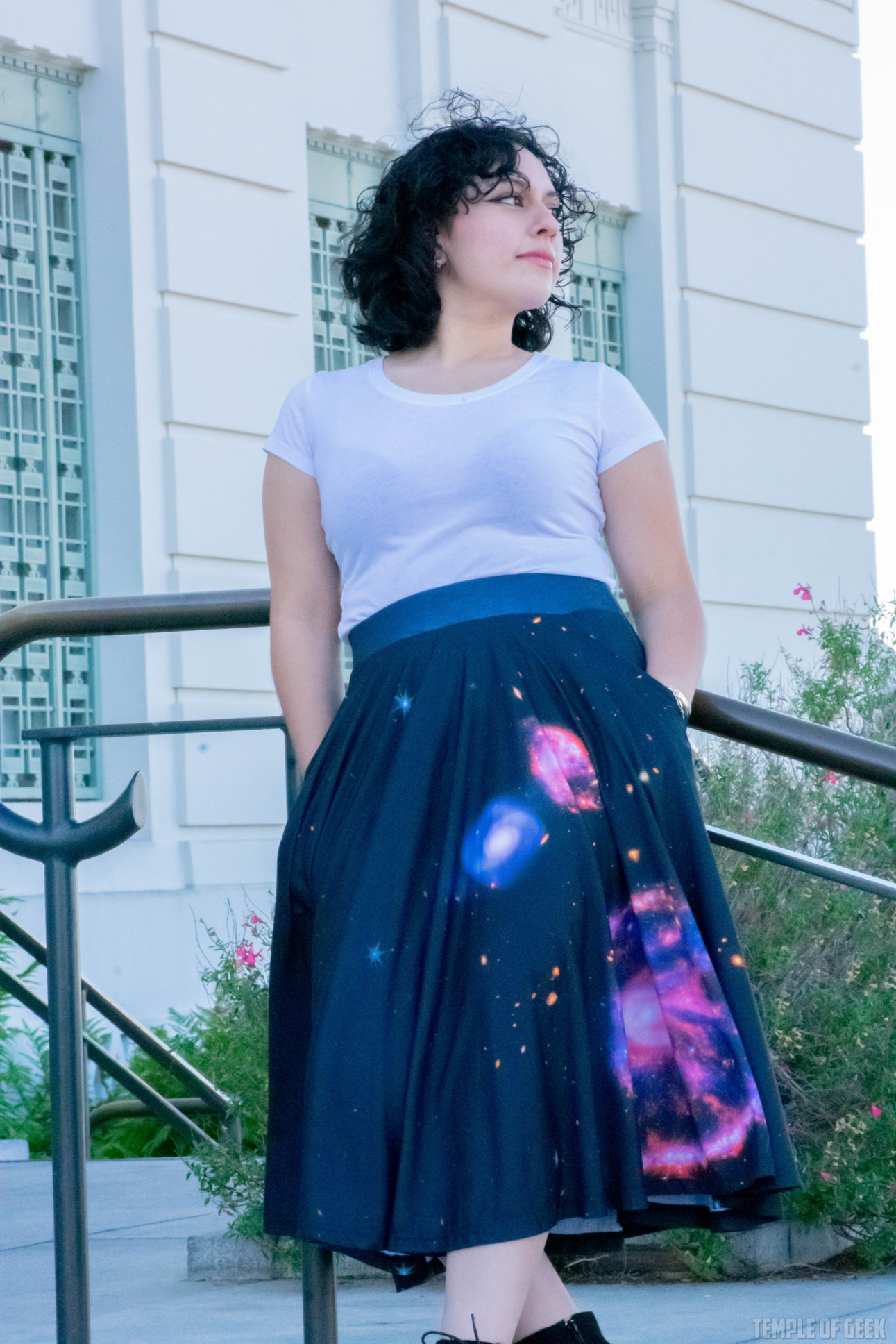 A model leans against a railing at Griffith Observatory. She wears a white tee with a black twirl skirt with galaxies on it.