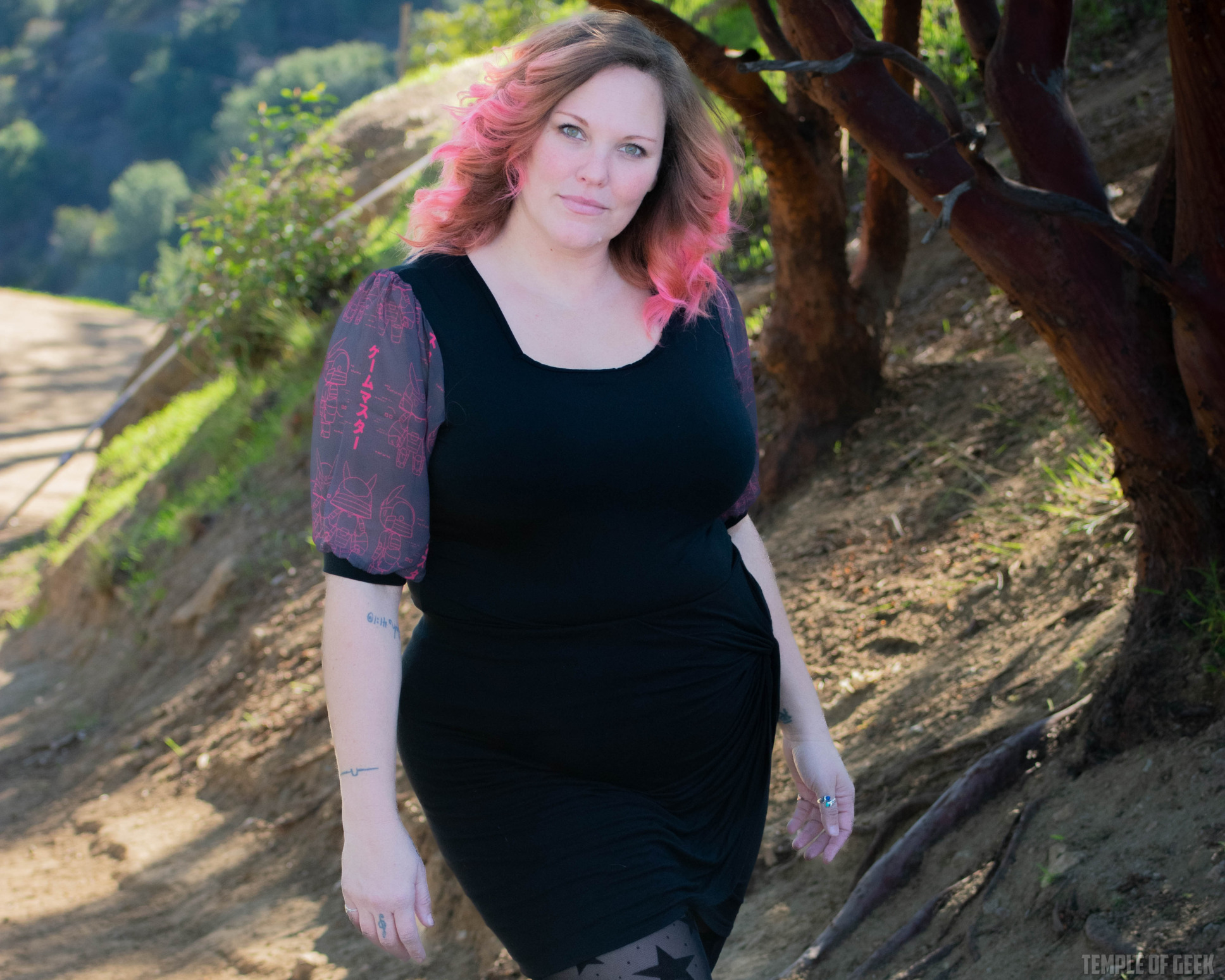 A model poses in a park wearing a black, gamer-themed top and a black skirt with tights with stars on them.