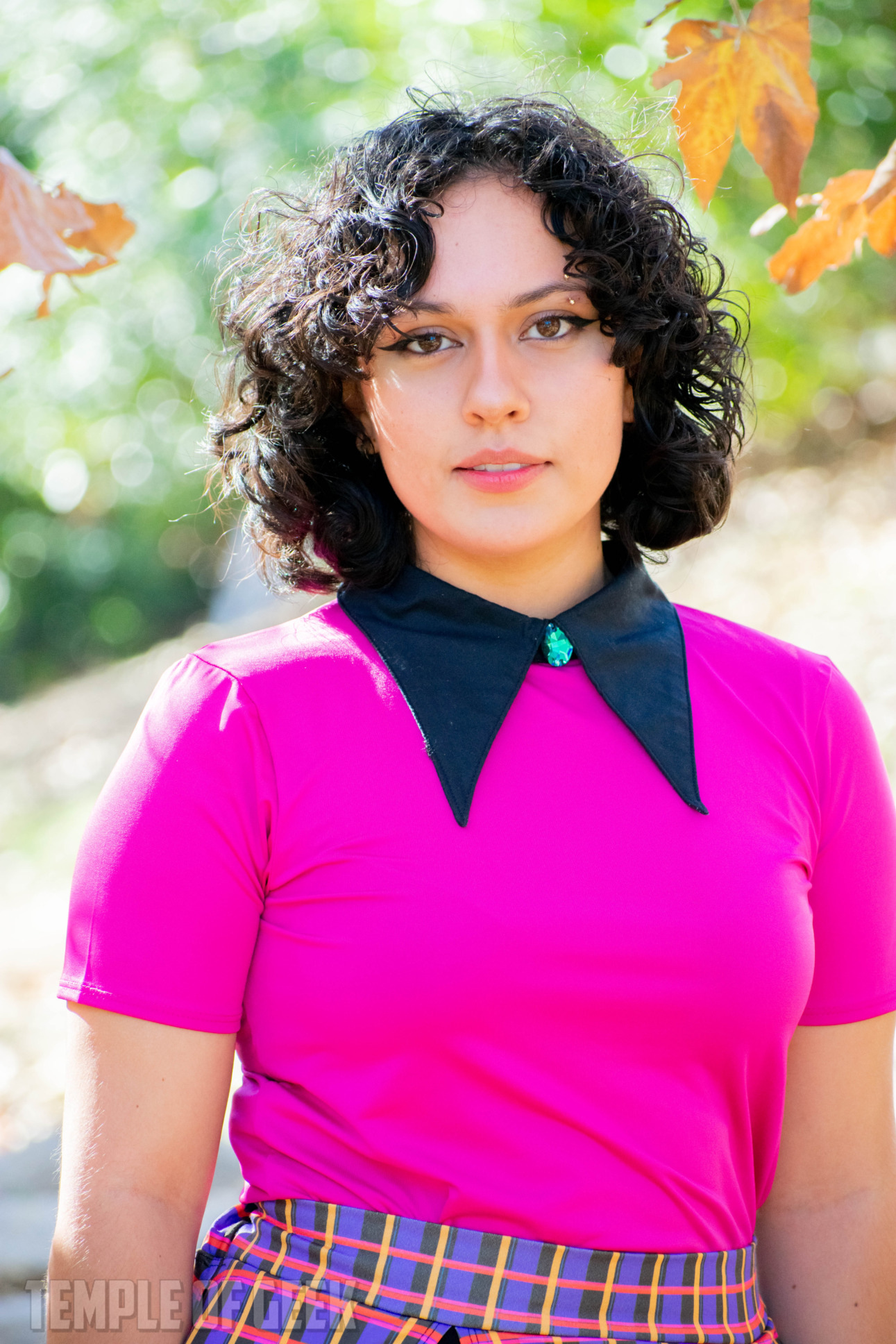 A model wears a magenta colored top with a pointed black collar, adorned with a blue gem, from GameMaster + Heroicouture.