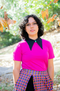 A model poses in a park wearing a magenta top and a plaid skort. 