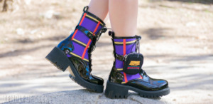 A closeup shot of a pair of vegan patent leather and plaid boots with a chunky heel and a small utlity belt with pouch. 