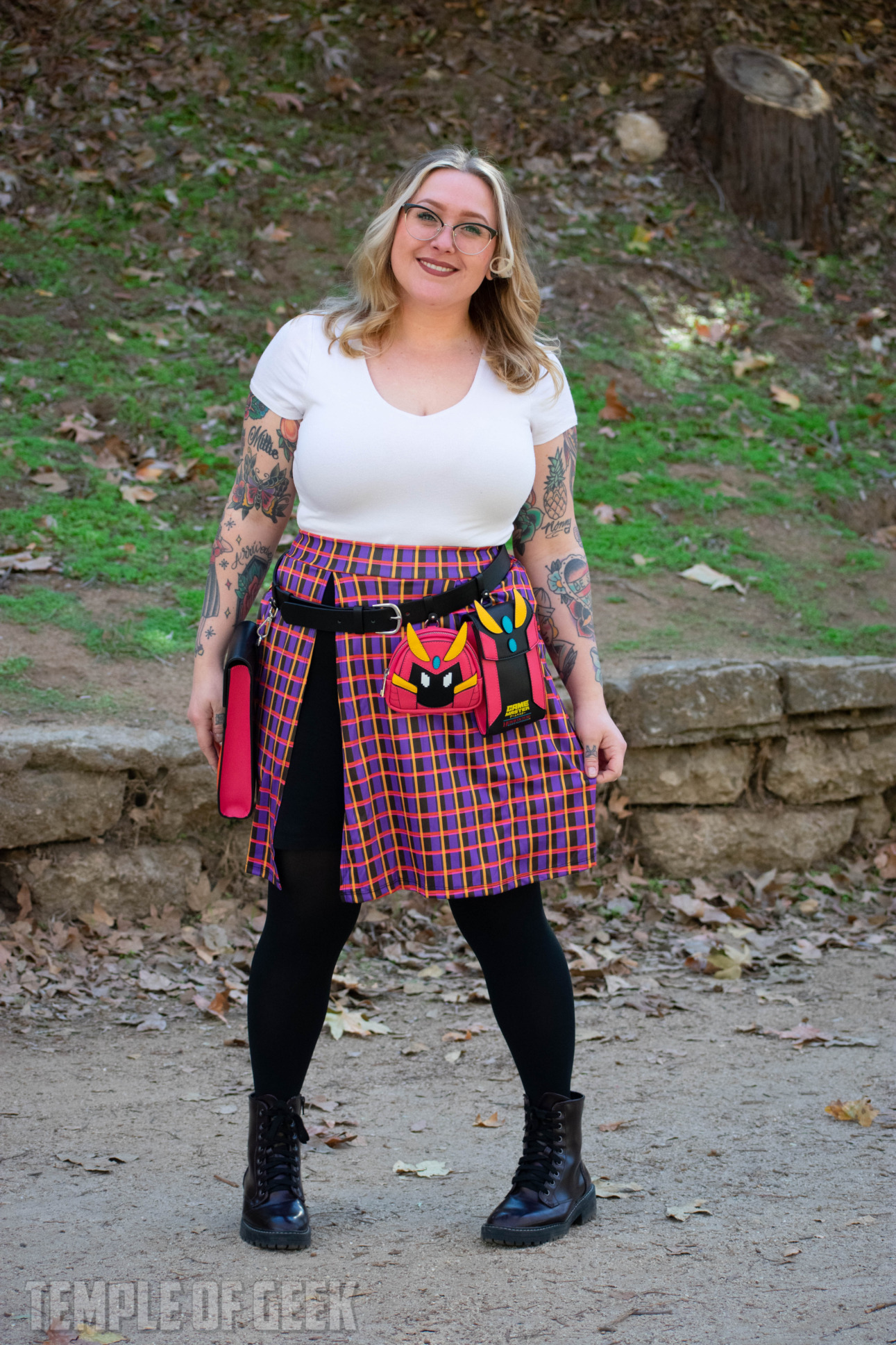 A model poses in a park wearing a plaid skort and a utility belt with attachable pouches themed after GameMaster mascot Hawk.