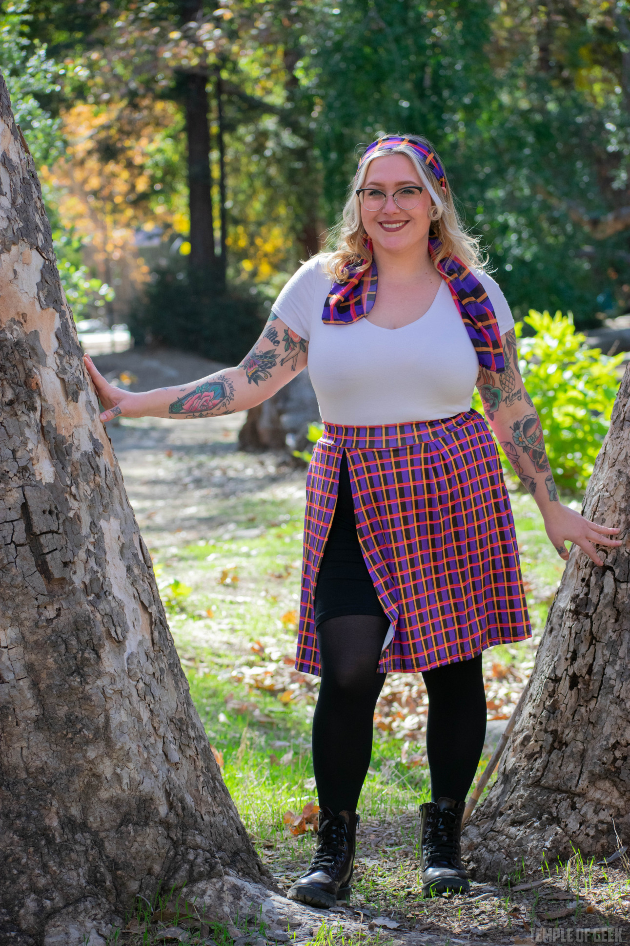 A model poses between the trunk of two trees, wearing a plaid skort from GameMaster + Heroiocouture.