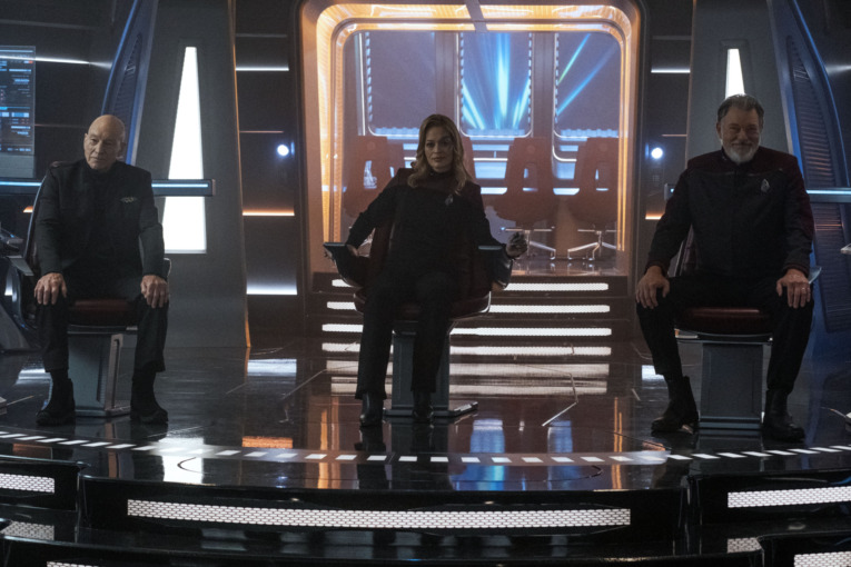 Jeri Ryan as Seven sits in the Captain's Chair Next to Jean Luc-Picard (Patrick Stewart) on her right and William Riker (Jonathan Frakes) on her left aboard the starship U.S.S. Titan-A. Star Trek: Picard season 3. 