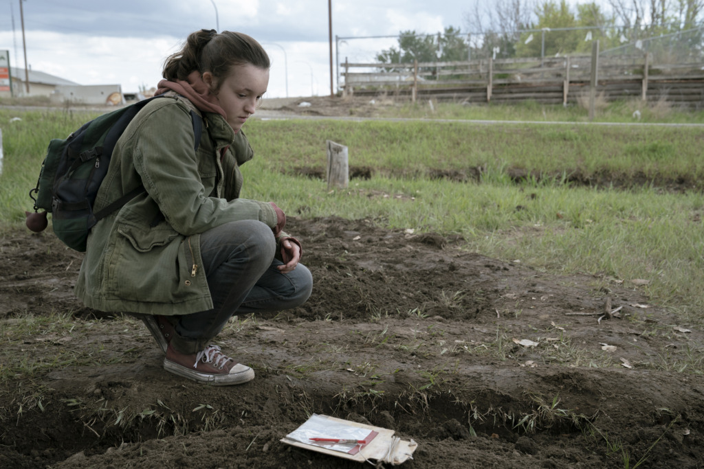 Ellie (Bella Ramsey) crouches next to Sam's grave.