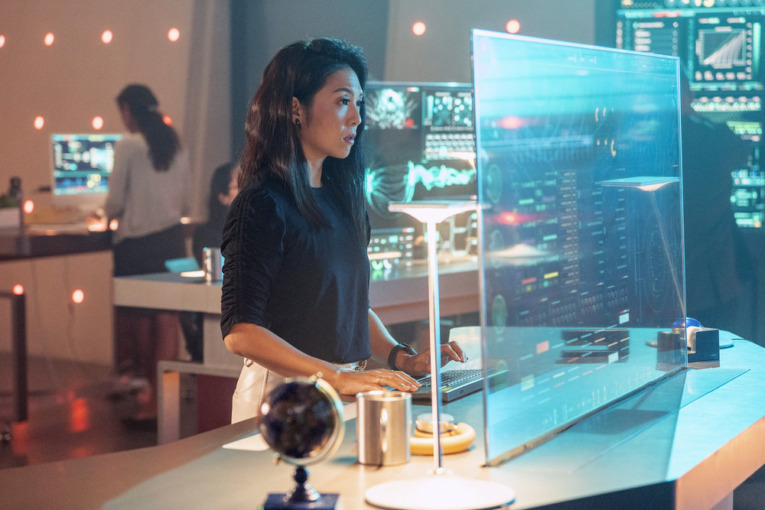 an image from the show Quantum Leap, Nanrisa Lee as Jenn stands at a futuristic computer and stares at the screen and she is typing. 