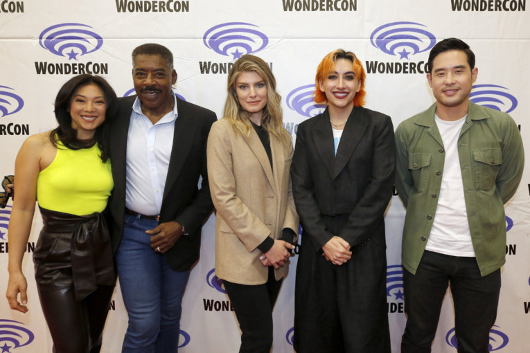 The cast a of Quantum Leap, Nanrisa Lee, Ernie Hudson, Caitlin Bassett, Mason Alexander Park, Raymond Lee pose smiling for photos against a WonderCon step and repeat background