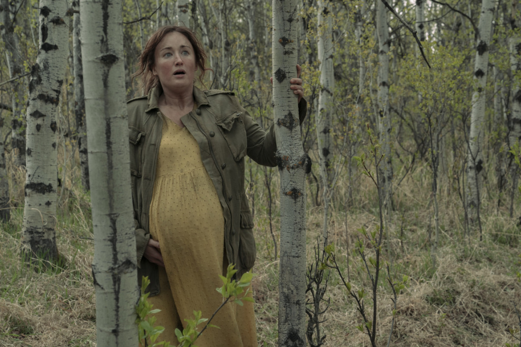 Heavily, pregnant, Anna (Ashley Johnson) stands in a forest/wood looking disheveled. 