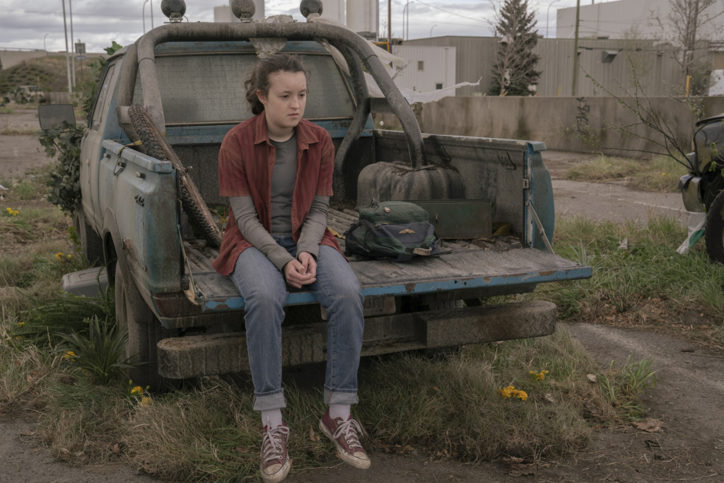 Ellie (Bella Ramsey) sits on a truck bed and stares off in the distance.