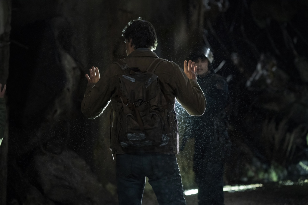 Joel (Pedro Pascal) stands with his hands up, facing a FEDRA soldier.