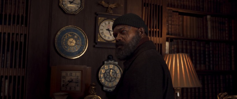 Nick Fury, dressed in a black long sleeved top and a black hat, stands in front of a wall of clocks. He is not wearing his signature eye patch and the eye injured in "Captain Marvel" is visible.