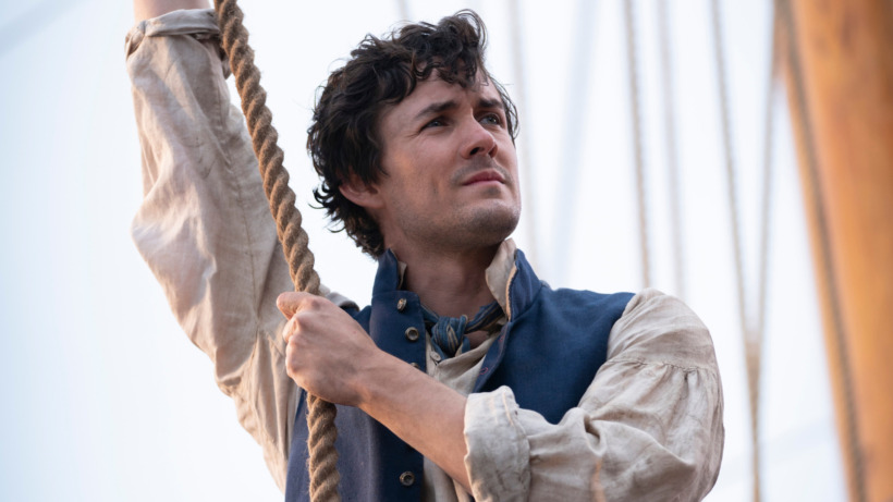 Jonah Hauer-King as Prince Eric in Disney's live-action THE LITTLE MERMAID. He is holding a rope for a sail on a ship. 