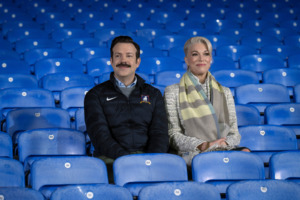 Jason Sudeikis and Hannah Waddingham sitting in football stadium seats for series Ted Lasso