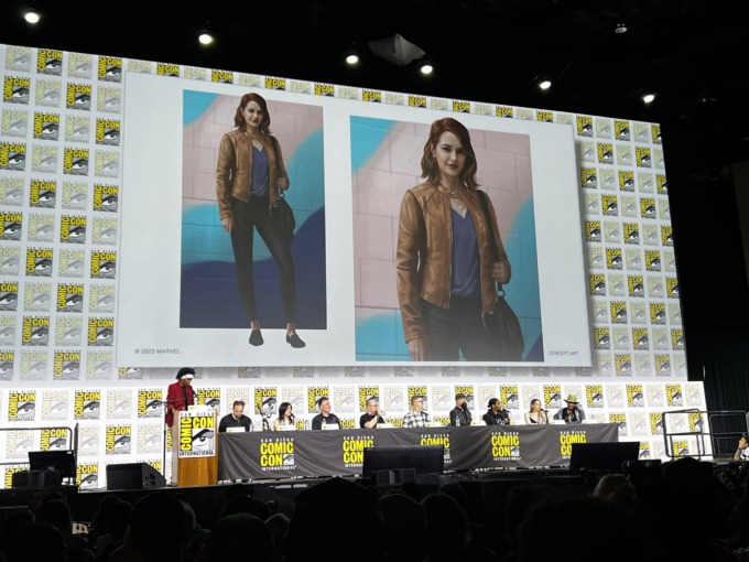 A look at MJ's new look at the Spider-Man 2 SDCC panel. Her hair is shorter and now worn loose instead of a ponytail. She wears a cropped light-tan leather jacket and a v-neck purple shirt with a delicate gold neckalce. She also has dark skinny jeans on, sensible shoes, and is carrying a messenger bag.