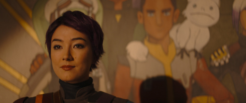 Sabine Wren, with short purple hair, stands in front of the mural she painted after the Battle of Lothal