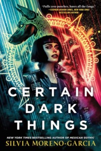 New cover for Silvia Moreno-Garcia's Certain Dark Things. Vibrant background with symbols. A dog and woman in front. The woman has short black hair and is wearing a leather jacket.