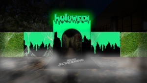 An entrance display in bright green and covered in spider webs. Huluween is in Halloween-inspired text, as a welcome mat reads "Now Screaming"