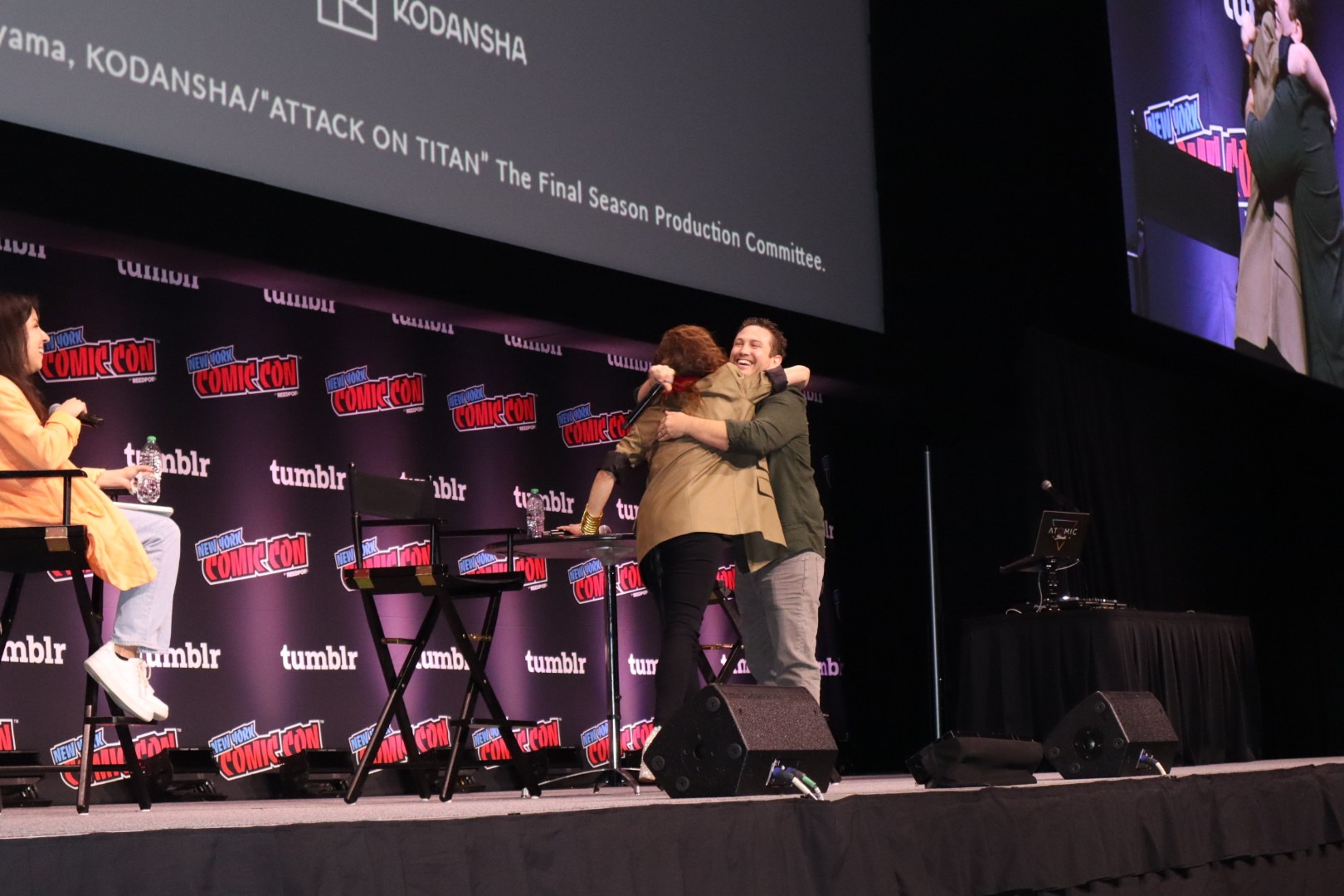 Bryce Papenbrook and Trina Nishimura embrace on stage for the Attack on Titan 10 Year Celebration and Dub panel at NYCC