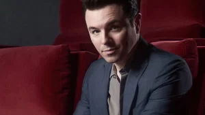 Seth MacFarlane in a suit sittinh in a theater 