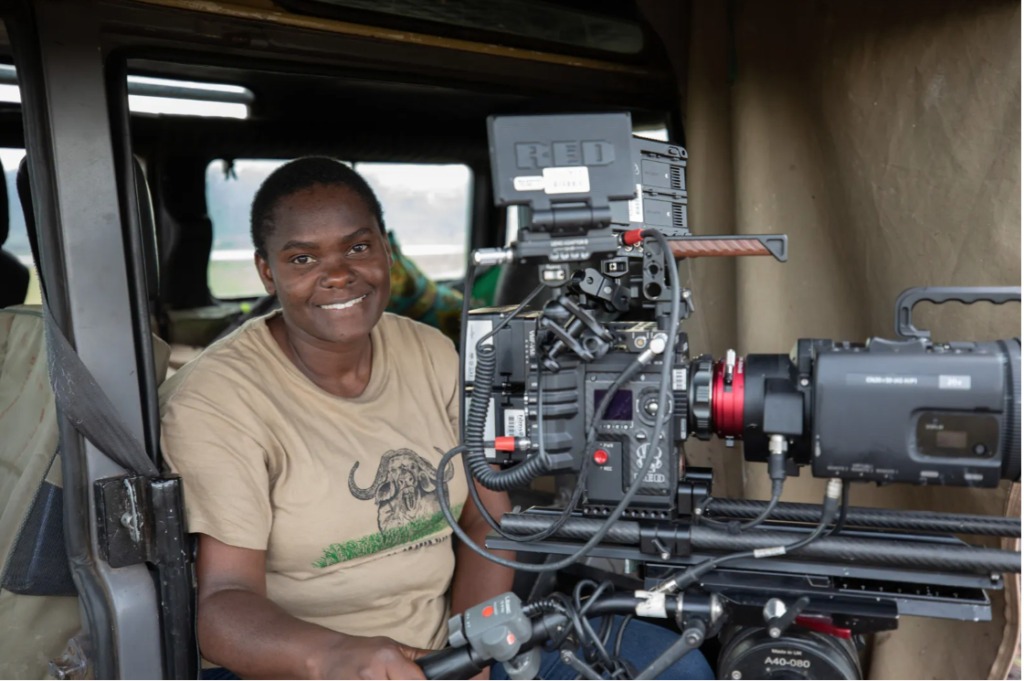 Erica Rugabandana sits behind a large camera.