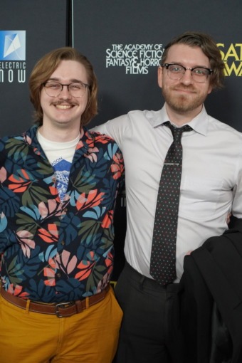 Photo of two men posing together on a red carpet.