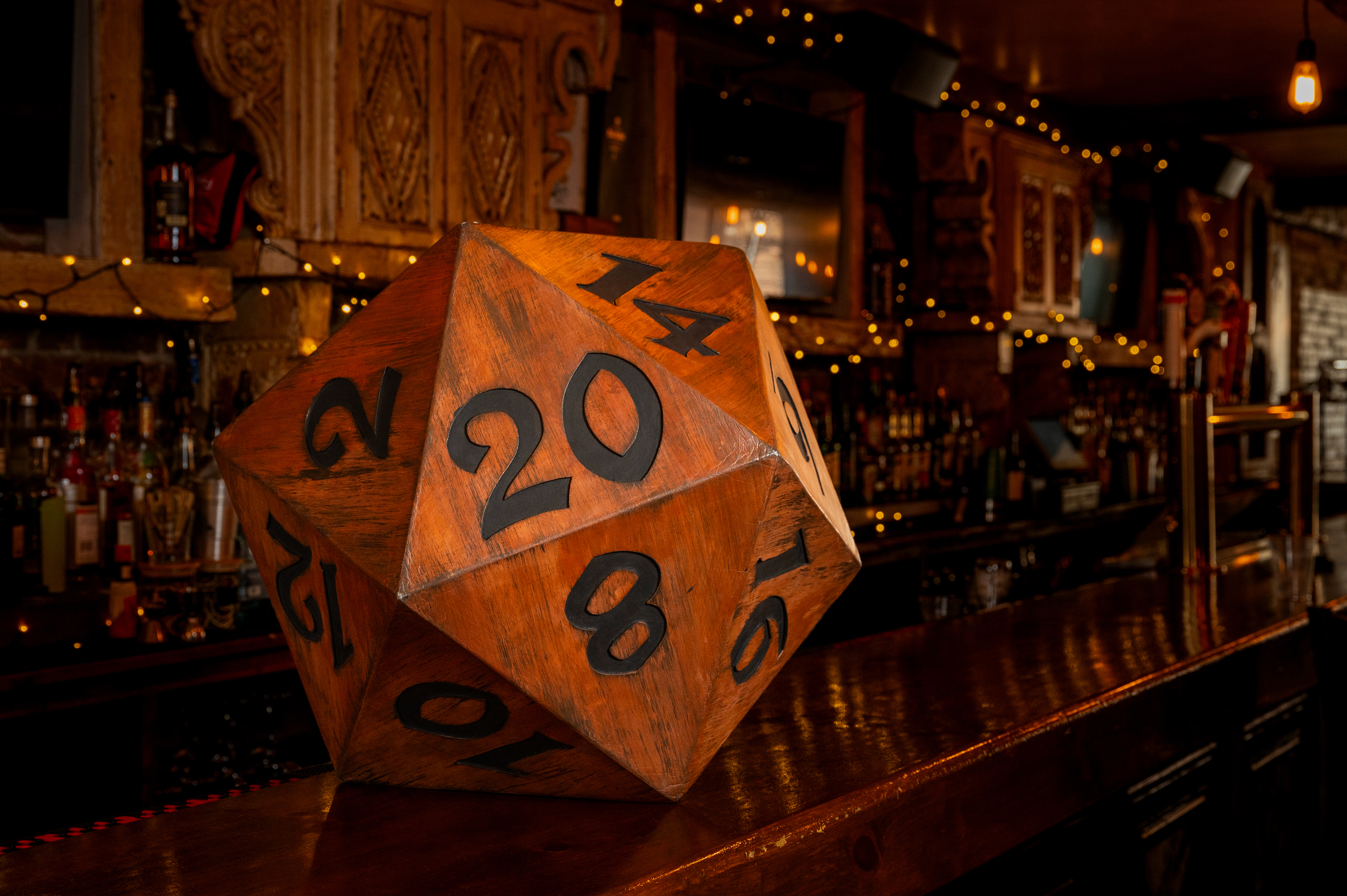 Giant Wooden D20 side with "20" facing forward on wooden bar counter.