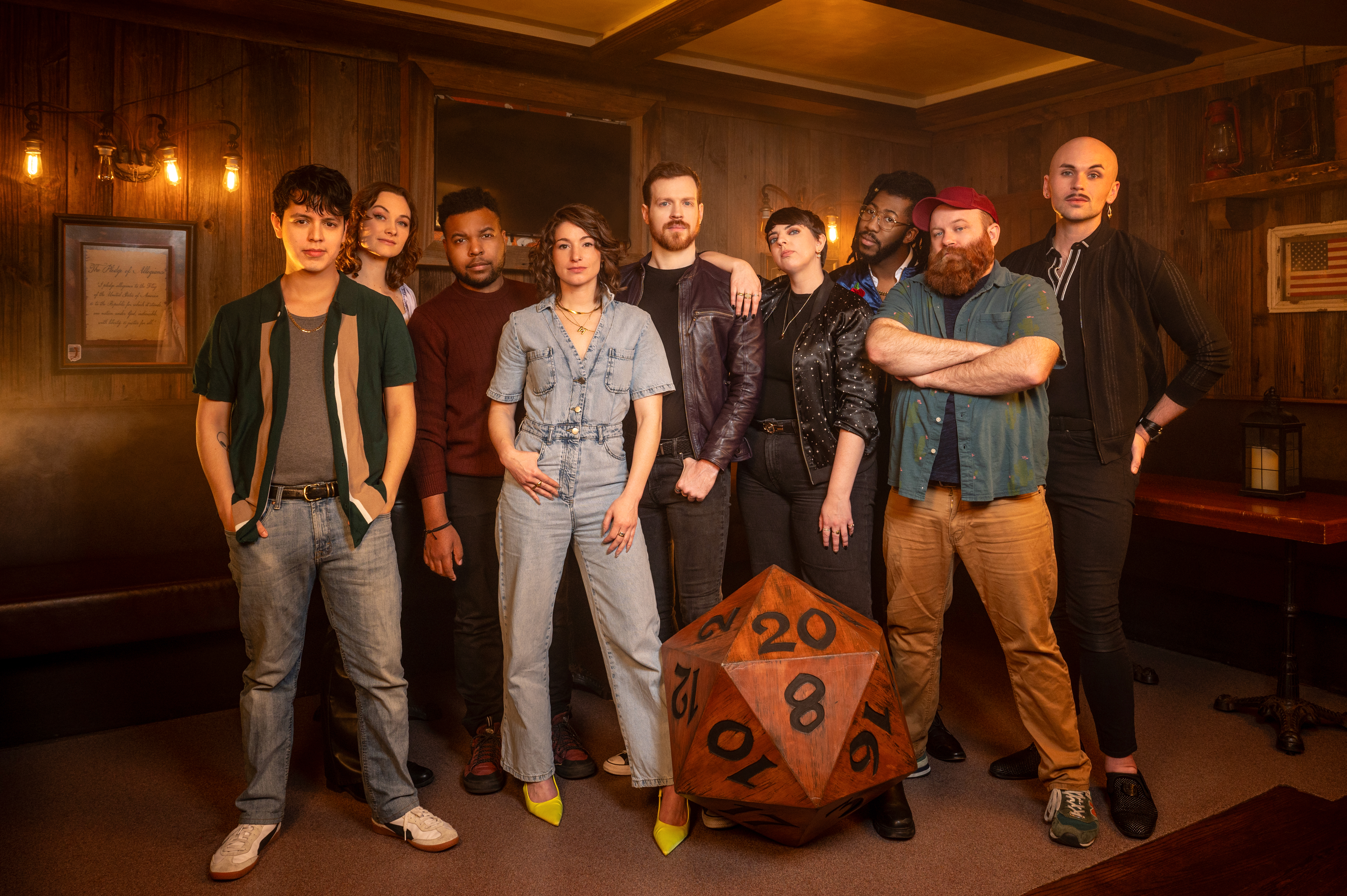 Group of nine individuals as the cast of Dungeons and Dragons "The Twenty-Sided Tavern" with a backdrop of a wood tavern.