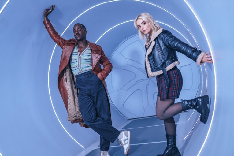 Ncuti Gatwa (The Doctor) and Millie Gibson (Ruby Sunday) pose in an interior, circular hallway of the TARDIS.